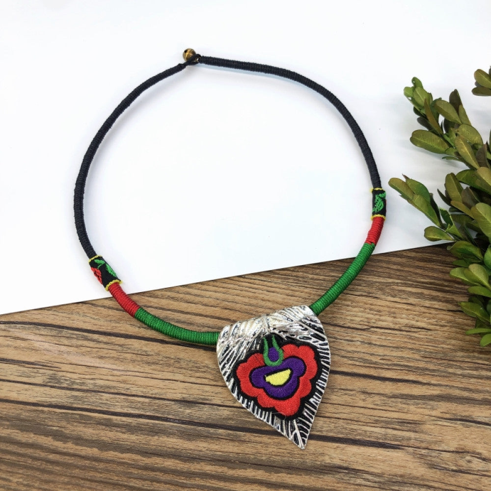 ethnic tri-color rope choker necklace, featuring a silver-tone ornate fringe pendant with colorful bead details, displayed on a wooden surface