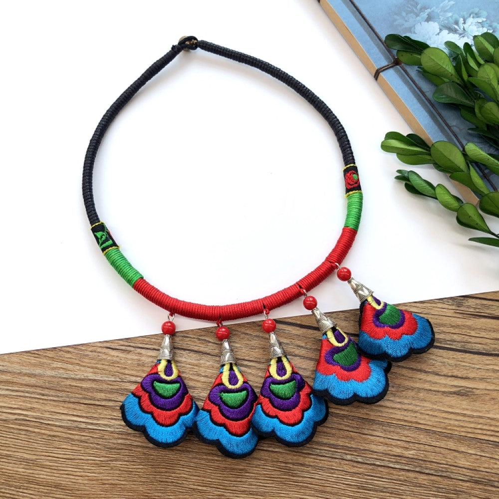 ethnic tri-color rope choker necklace, featuring a silver-tone ornate fringe pendant with colorful bead details, displayed on a wooden surface 01