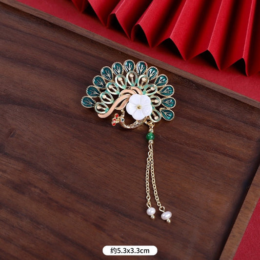 This elegant brooch features a delicate fan-shaped design, crafted with a gold-tone metal frame and adorned with vibrant multicolored gemstones. A lustrous pearl anchors the center, from which three graceful gold chains dangle, each finished with a small pearl drop. Perfect for adding a touch of sophistication to blazers, scarves, or special occasion outfits, this piece blends intricate craftsmanship with timeless, eye-catching charm. 01