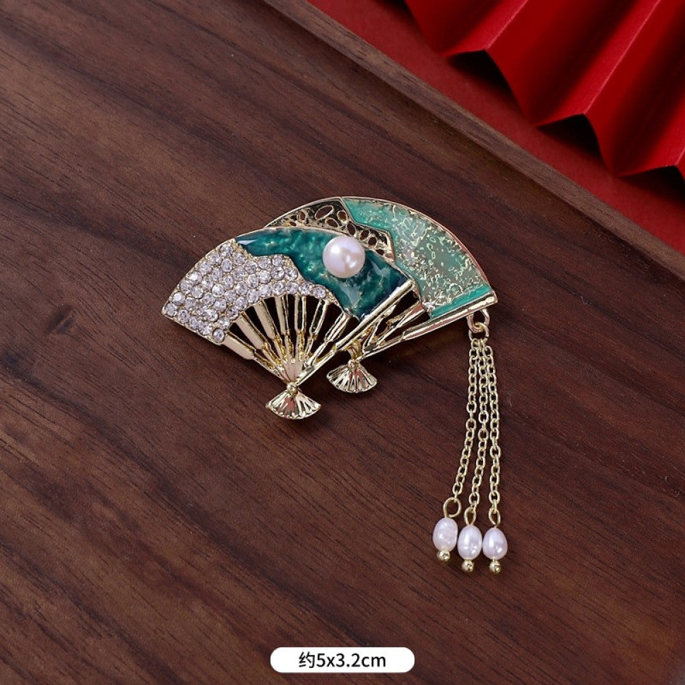 This elegant brooch features a delicate fan-shaped design, crafted with a gold-tone metal frame and adorned with vibrant multicolored gemstones. A lustrous pearl anchors the center, from which three graceful gold chains dangle, each finished with a small pearl drop. Perfect for adding a touch of sophistication to blazers, scarves, or special occasion outfits, this piece blends intricate craftsmanship with timeless, eye-catching charm 30