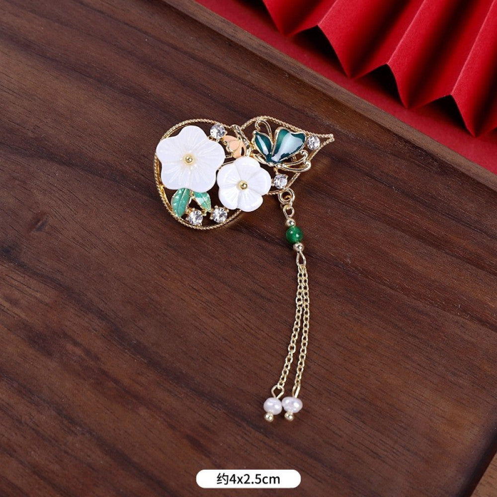 This elegant brooch features a delicate fan-shaped design, crafted with a gold-tone metal frame and adorned with vibrant multicolored gemstones. A lustrous pearl anchors the center, from which three graceful gold chains dangle, each finished with a small pearl drop. Perfect for adding a touch of sophistication to blazers, scarves, or special occasion outfits, this piece blends intricate craftsmanship with timeless, eye-catching charm 05
