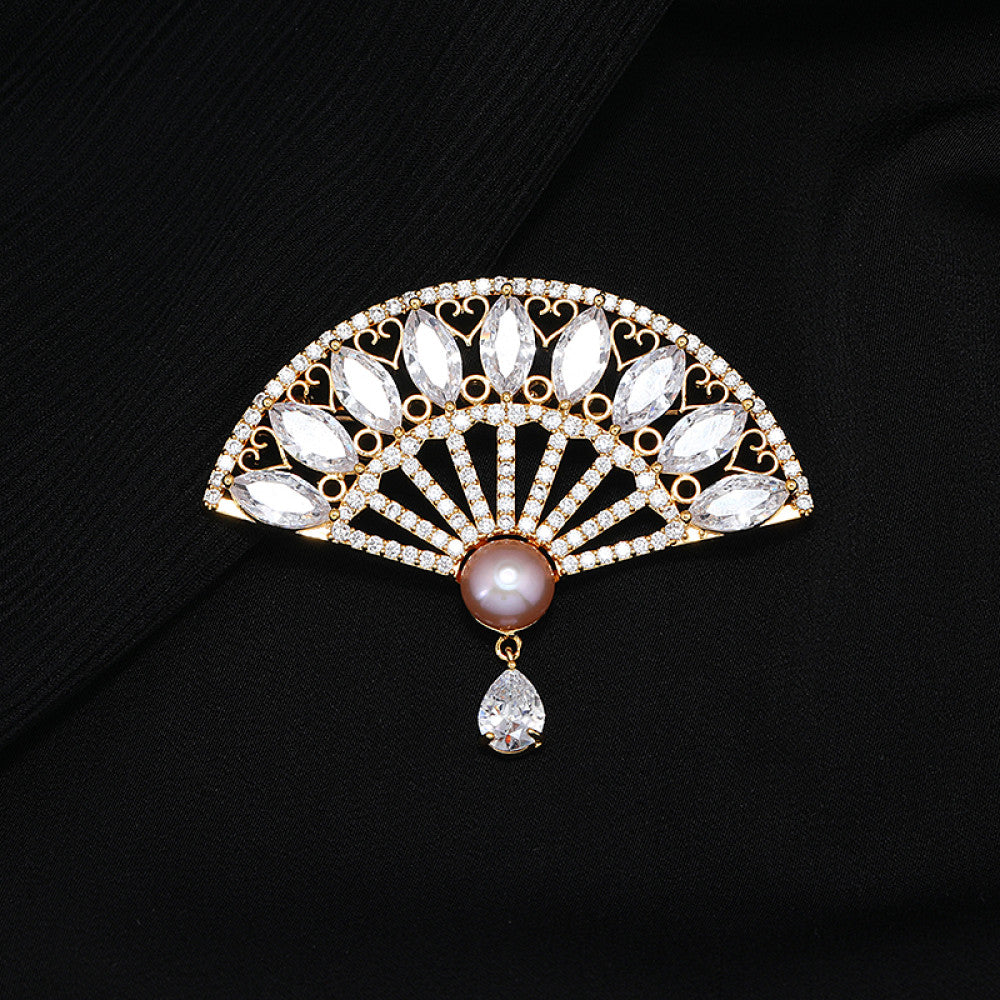 This elegant brooch features a striking fan-shaped design, crafted with a gold-tone metal base. It is adorned with vibrant emerald-green gemstones, shimmering clear crystals, and a lustrous pearl at the center, from which a teardrop-shaped green gem dangles gracefully. Perfect for adding a touch of sophistication to blazers, scarves, or evening wear, this piece blends timeless elegance with a bold, eye-catching silhouette.01