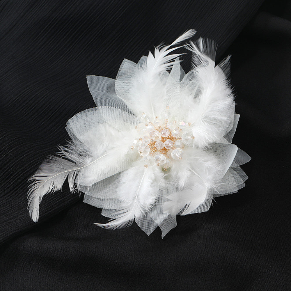 This hair accessory features light white feathers and sheer tulle, layered like a blooming flower. The center is adorned with sparkling crystals and pearls, creating a dreamy, ethereal look perfect for bridal styles or special occasions.