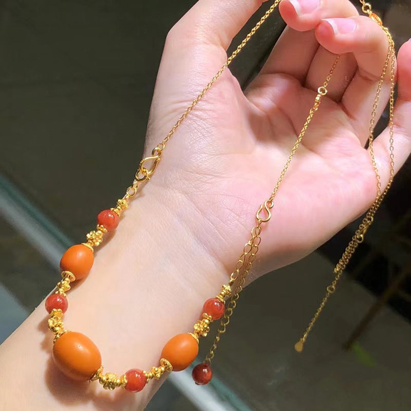 A hand - held necklace featuring a gold chain, with large old - style beeswax beads and small South Red Agate beads as accents, suitable for adding an elegant touch to any outfit.
