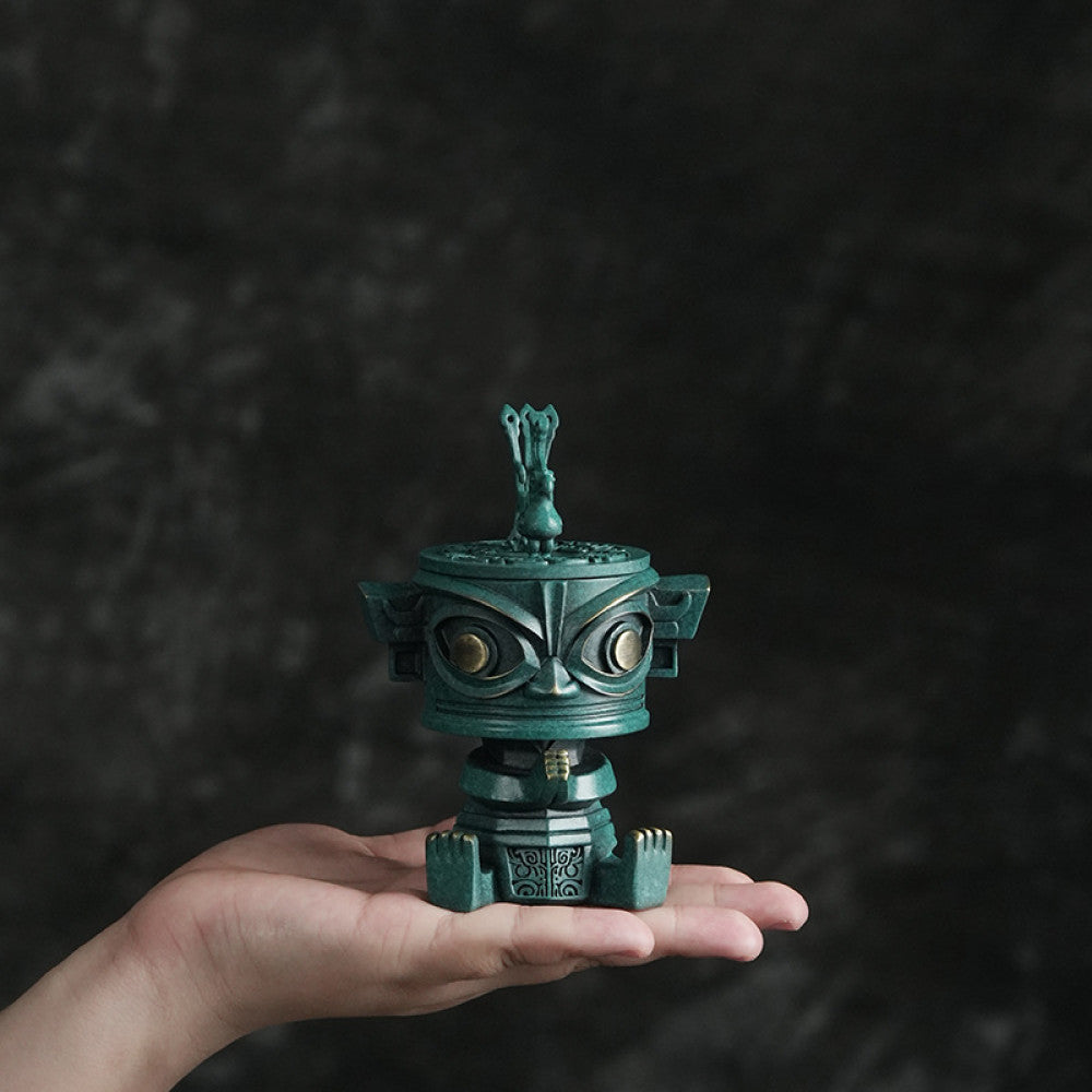 A small bronze-style incense burner being held in one hand against a dark backdrop.
