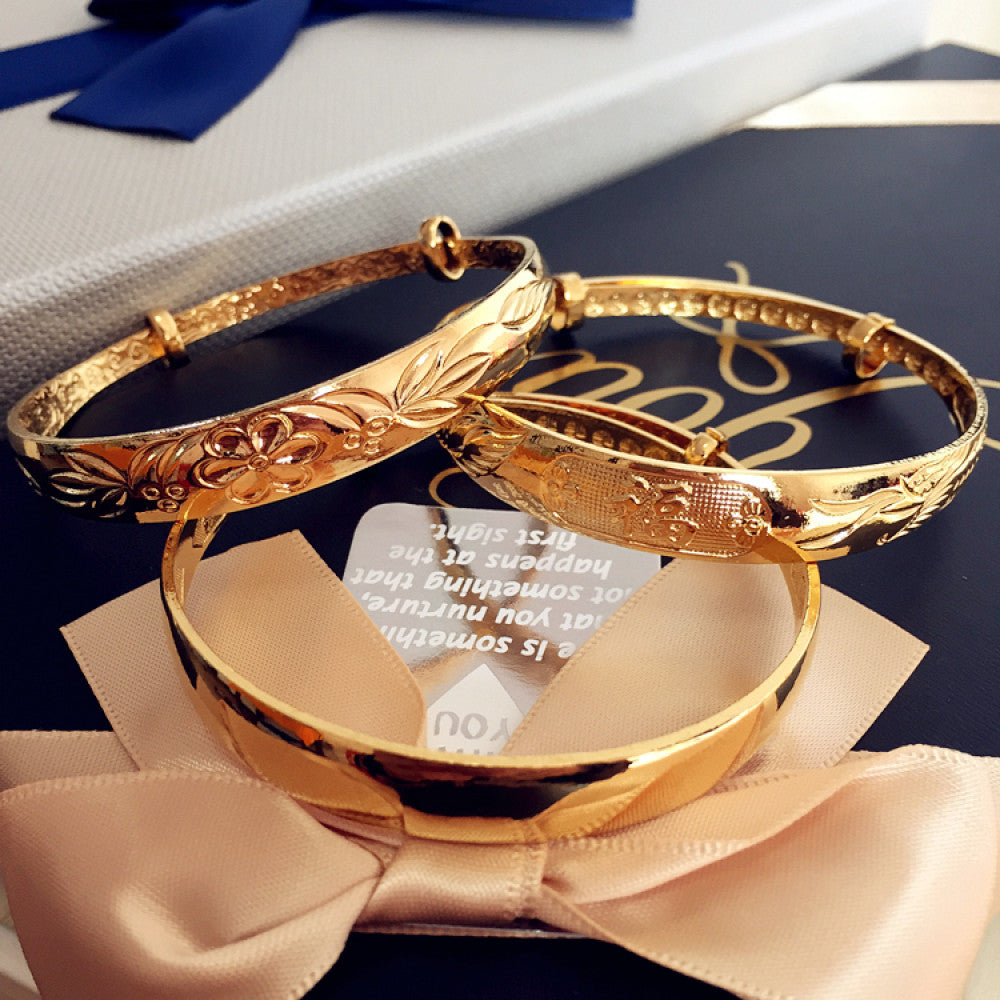 Luxury gold-tone bangle set with engraved floral and sleek designs, displayed on gift packaging with a bow, ideal for luxury fashion and gifting enthusiasts