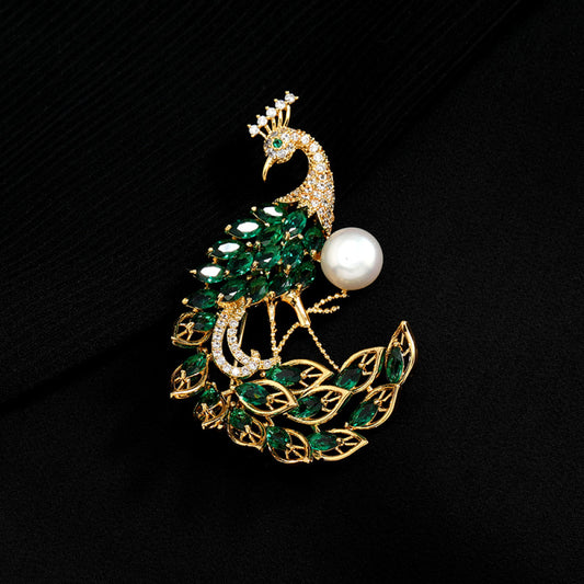 This opulent brooch showcases a majestic peacock design, crafted with a gleaming gold-tone metal base. The peacock’s body and elaborate tail are lavishly adorned with vibrant emerald-cut green crystals, while its head and neck are encrusted with sparkling clear crystals. A large, lustrous white pearl rests gracefully beside the peacock, adding a touch of timeless elegance. Perfect for elevating formal attire, evening gowns, or special occasion outfits, this statement piece exudes luxury and intricate crafts