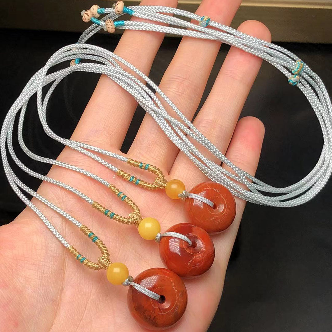 A set of necklaces featuring Nanhong agate peace buttons, paired with beeswax beads and turquoise accents, held in a hand.