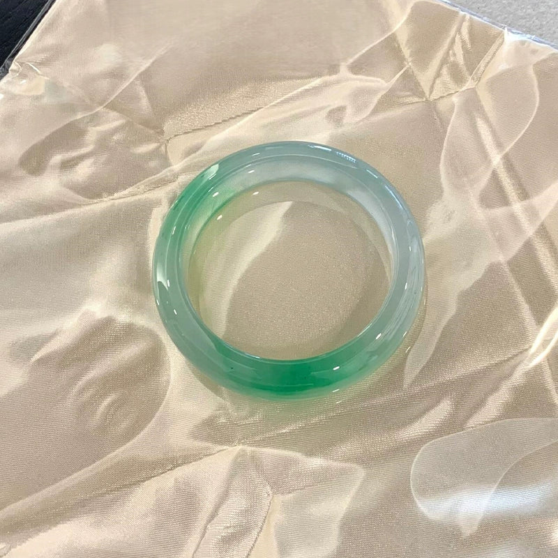 Natural icy jadeite bangle with vivid green accents placed on silky fabric 