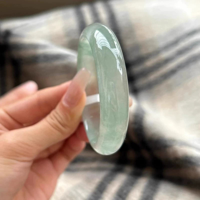 Hand holding natural icy light green jade bangle against plaid fabric