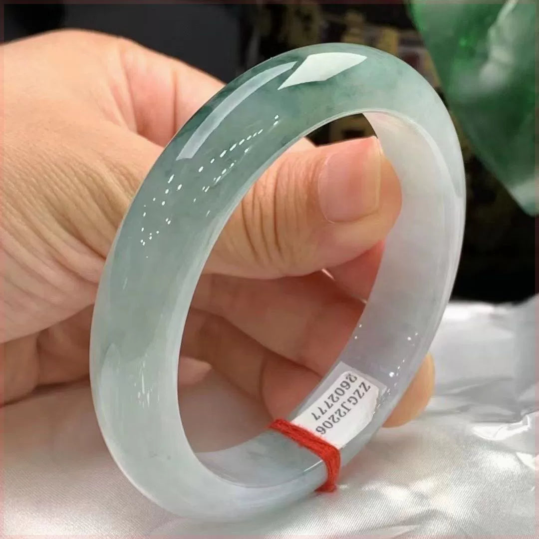 Hand holding natural icy light green jadeite bangle with red string 