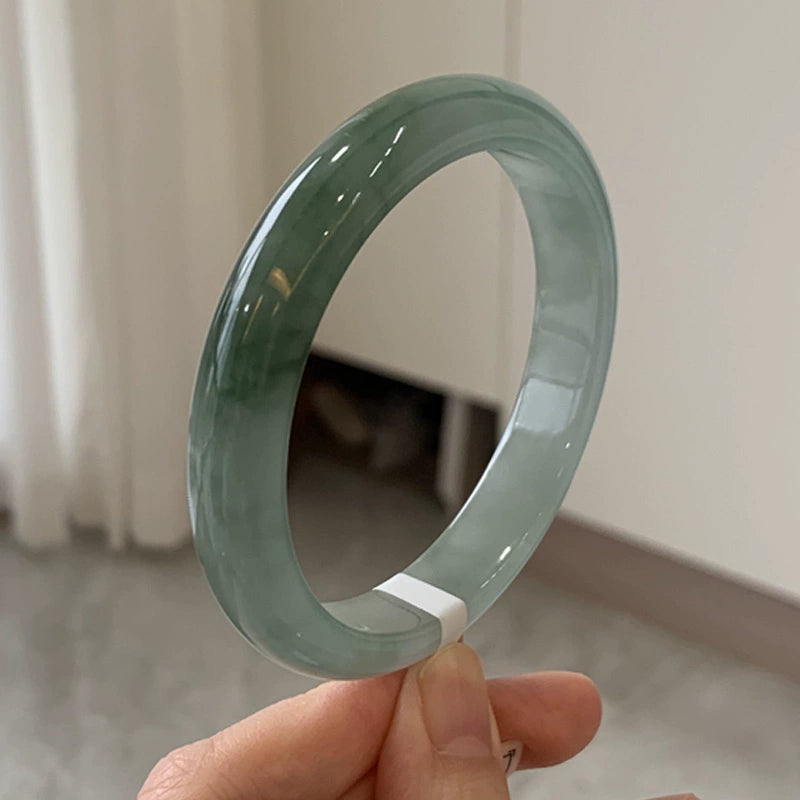 Hand holding natural light green jadeite bangle with glossy surface in indoor setting