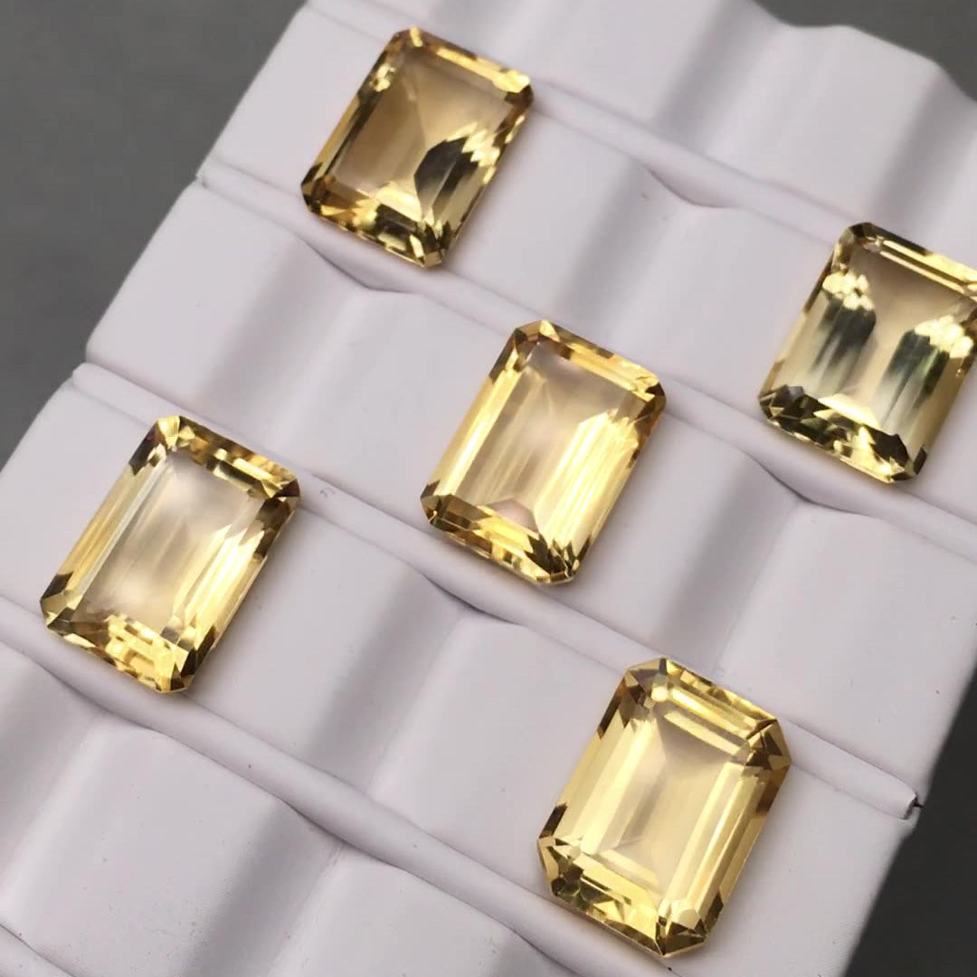 Five rectangular-cut golden yellow gemstone rough stones displayed on a white display rack.