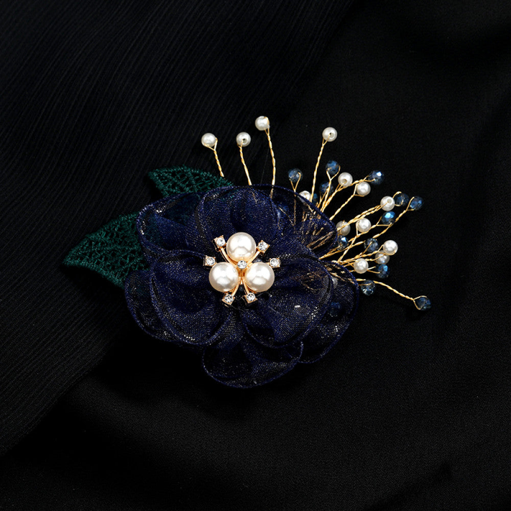 This elegant accessory features a layered navy tulle flower at its center, adorned with lustrous pearls and sparkling crystals. Delicate gold wire sprigs dotted with white and blue beads extend outward, complemented by a rich green lace leaf. Perfect for adding a touch of sophistication to evening gowns, blazers, or special occasion outfits, this piece blends delicate craftsmanship with timeless elegance.