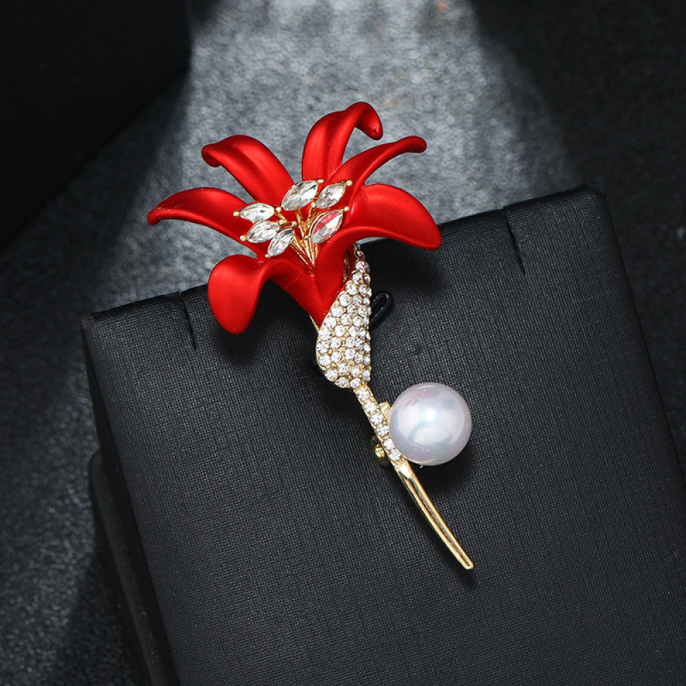 This elegant brooch features a vibrant red lily with a crystal-encrusted gold stem, accented by a lustrous pearl. A sophisticated floral accessory for any outfit