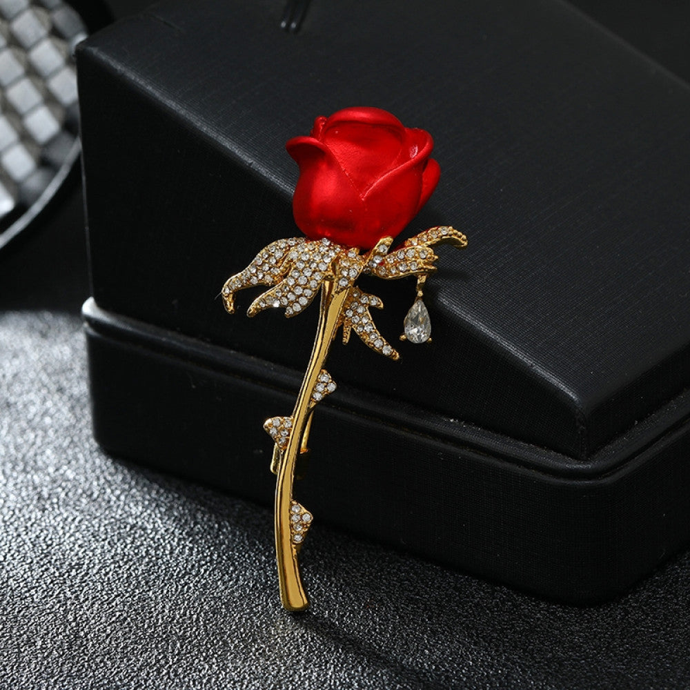 This elegant brooch features a vivid red rose with a gold crystal-encrusted stem, accented by a delicate teardrop detail. A romantic accessory to elevate any outfit 01