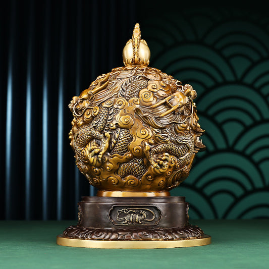 Brass decorative ball statue with intricate dragon and cloud carvings, wooden base, against traditional Chinese patterned background on green surface