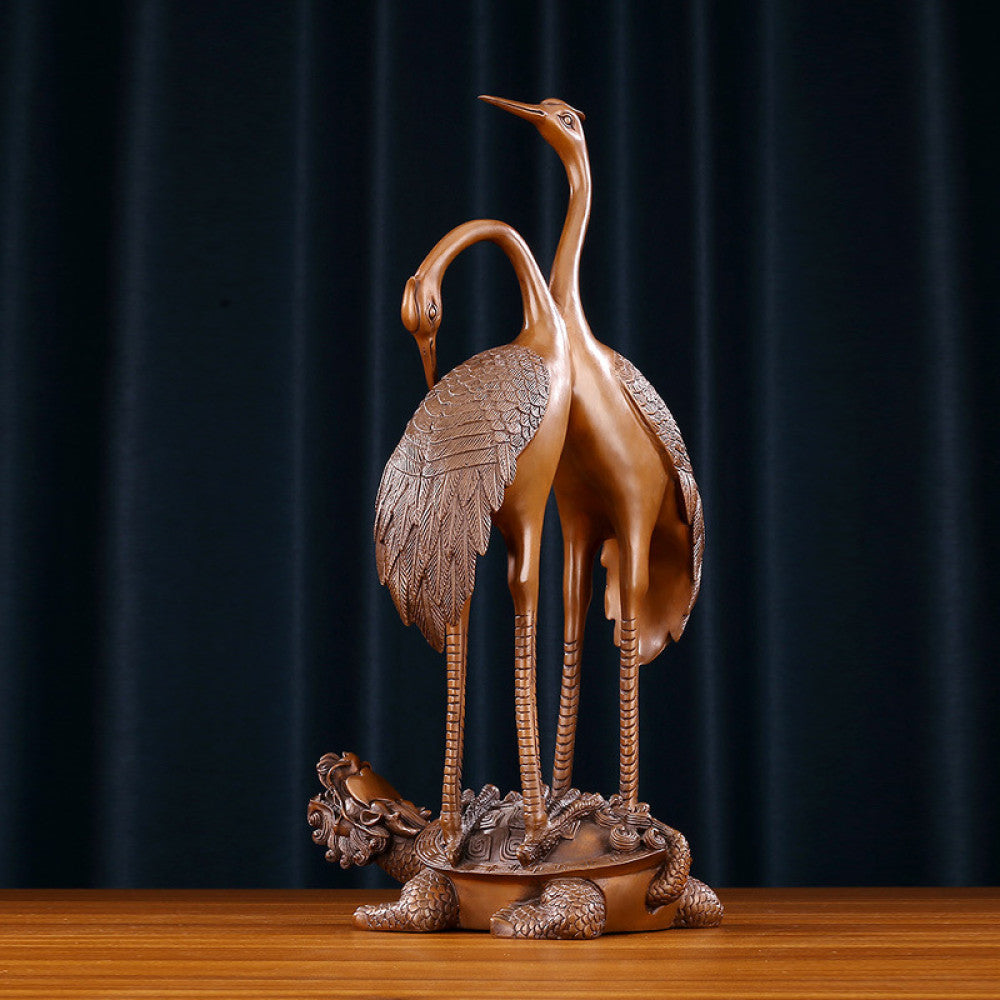 Traditional Chinese bronze crane pair statue with intertwined necks, standing on a dragon turtle base against a dark blue curtain background