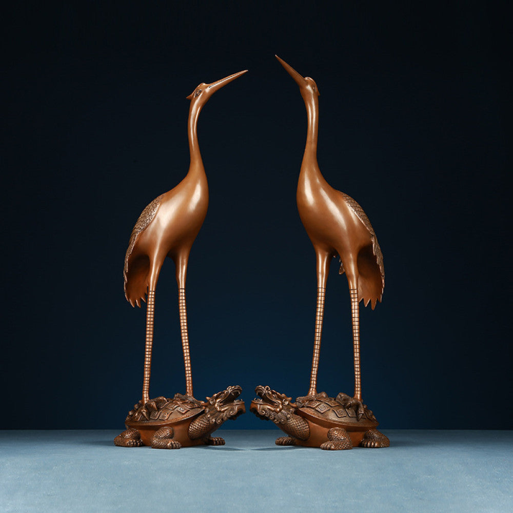 Pair of traditional Chinese bronze crane statues standing on tortoises, displayed against a dark blue background
