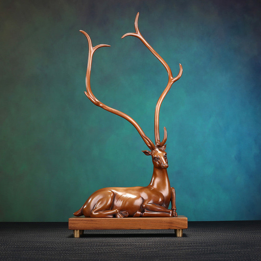Traditional Chinese bronze deer statue with long antlers, lying on a wooden base against a teal and brown gradient background