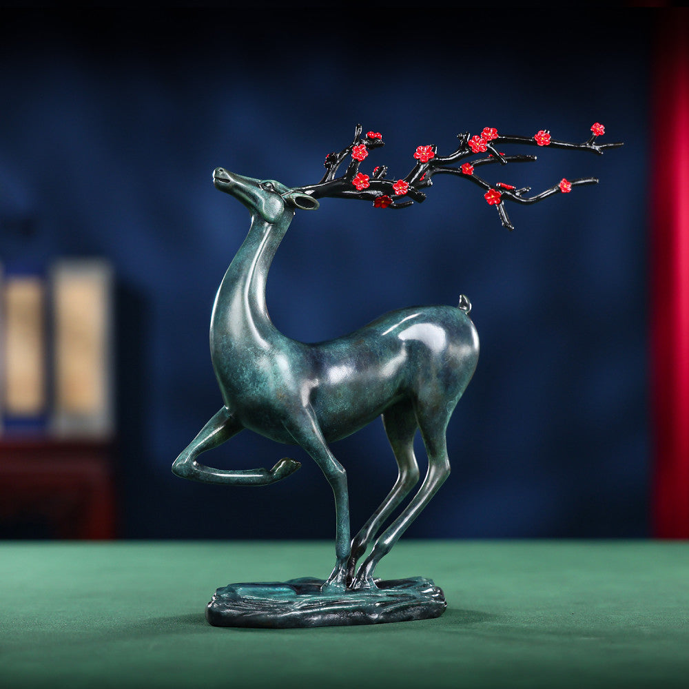Traditional Chinese bronze deer statue with red plum blossom branch, in an elegant pose, placed on a green surface against a dark blue background 01
