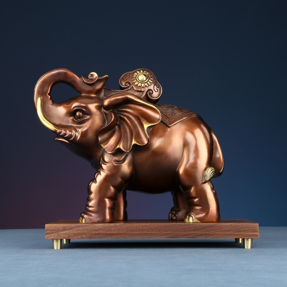 Traditional Chinese bronze elephant statue with golden details, curled trunk, and auspicious design on back, placed on a wooden base against a dark blue gradient background
