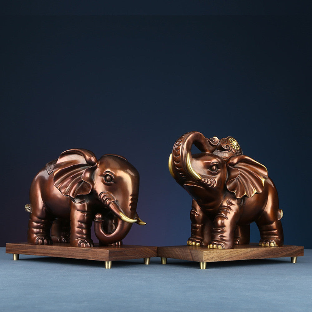 Pair of traditional Chinese bronze elephant statues with golden details, one with a curled trunk and one holding an ornament, placed on wooden bases against a dark blue background
