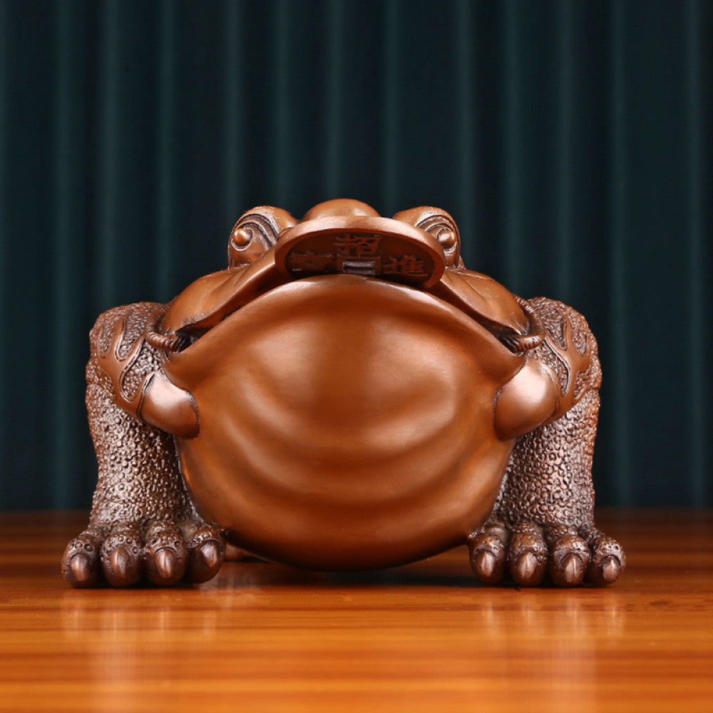 Traditional Chinese bronze money toad statue with a copper coin in its mouth, positioned on a wooden surface against a dark curtain background 02