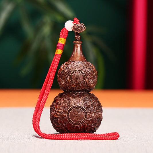 Traditional Chinese carved wooden gourd ornament with intricate patterns and red cord, placed against a blurred green plant background