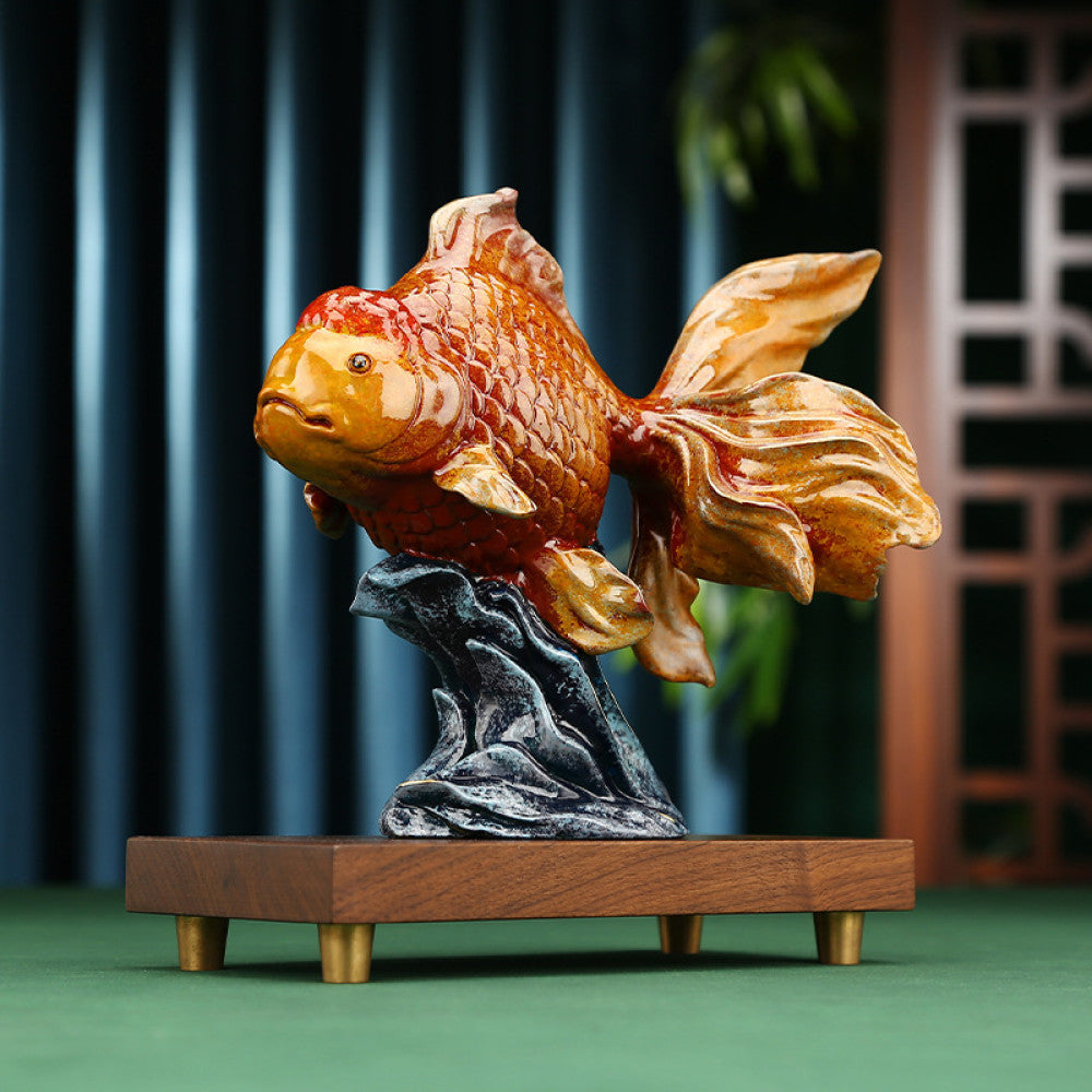 Colorful traditional Chinese goldfish statue with detailed scales, placed on a wooden base with a rocky stand, against a dark blue curtain and Chinese lattice background
