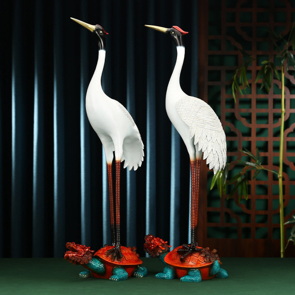 Pair of traditional Chinese crane statues standing on colorful tortoises, set against a dark screen with Chinese lattice design background