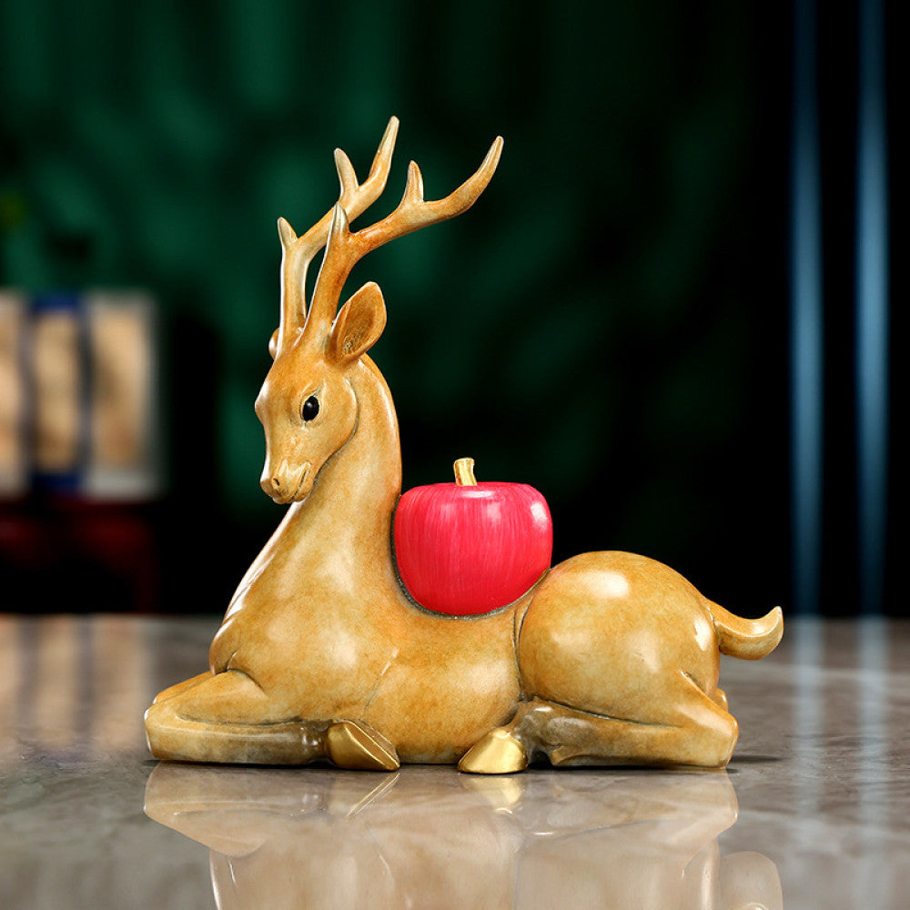 Traditional Chinese golden deer statue lying down with a red apple, placed on a glossy surface against a dark green background