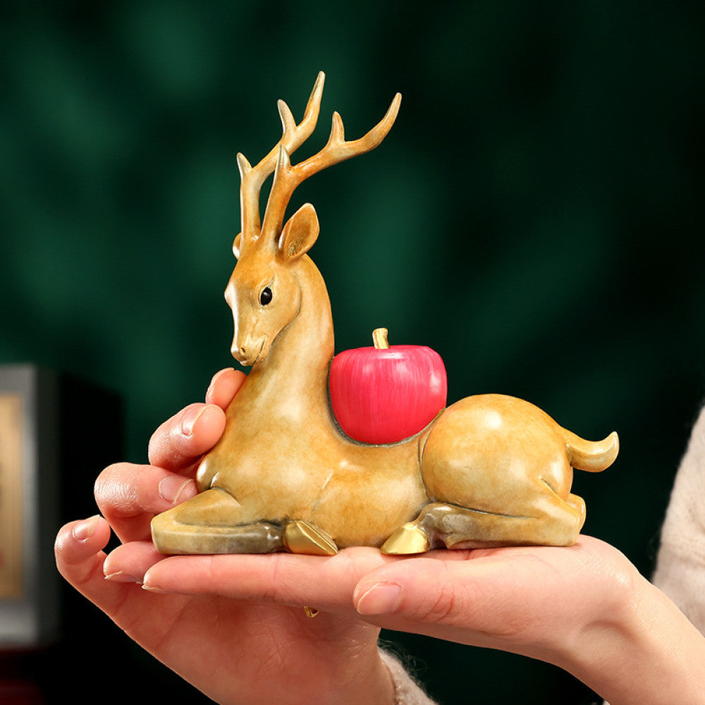 Traditional Chinese golden deer statue lying down with a red apple, placed on a glossy surface against a dark green background 01