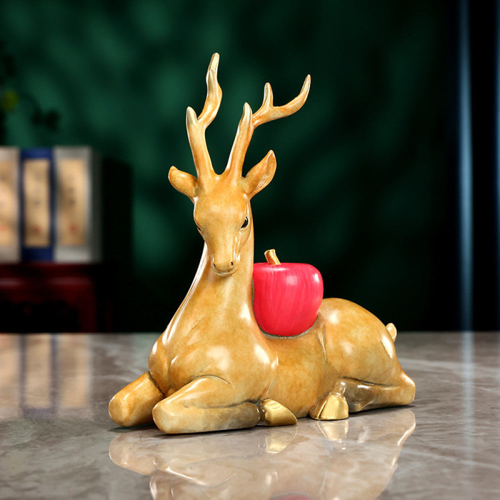 Traditional Chinese golden deer statue lying down with a red apple, placed on a glossy surface against a dark green background 02