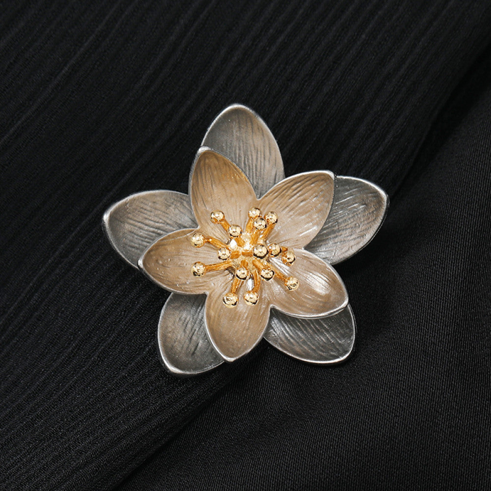 This elegant floral brooch features a striking two-tone metal design, with silver-toned outer petals and warm gold inner petals showcasing a delicate, brushed texture. The center is adorned with a cluster of sparkling clear crystals, adding a touch of luminous sophistication. Perfect for elevating blazers, scarves, or everyday outfits, this piece blends modern design with timeless floral charm.
