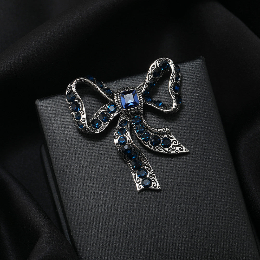 This eye-catching brooch features a classic bow design, crafted with an antiqued gold-tone metal base intricately adorned with vibrant red crystals. A large, faceted red gemstone anchors the center, while delicate filigree detailing adds vintage charm. Perfect for elevating blazers, scarves, or festive outfits, this bold piece brings a touch of glamorous retro style to any look 01