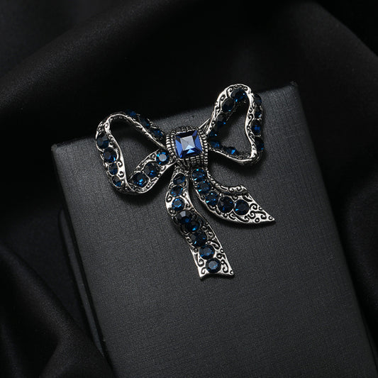 This eye-catching brooch features a classic bow design, crafted with an antiqued gold-tone metal base intricately adorned with vibrant red crystals. A large, faceted red gemstone anchors the center, while delicate filigree detailing adds vintage charm. Perfect for elevating blazers, scarves, or festive outfits, this bold piece brings a touch of glamorous retro style to any look 01