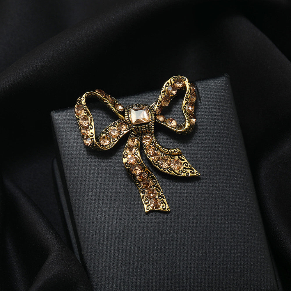 This eye-catching brooch features a classic bow design, crafted with an antiqued gold-tone metal base intricately adorned with vibrant red crystals. A large, faceted red gemstone anchors the center, while delicate filigree detailing adds vintage charm. Perfect for elevating blazers, scarves, or festive outfits, this bold piece brings a touch of glamorous retro style to any look 02