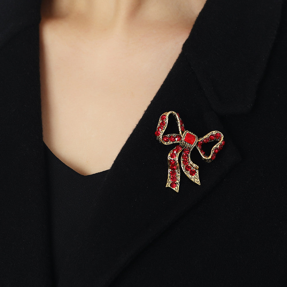 This eye-catching brooch features a classic bow design, crafted with an antiqued gold-tone metal base intricately adorned with vibrant red crystals. A large, faceted red gemstone anchors the center, while delicate filigree detailing adds vintage charm. Perfect for elevating blazers, scarves, or festive outfits, this bold piece brings a touch of glamorous retro style to any look 03
