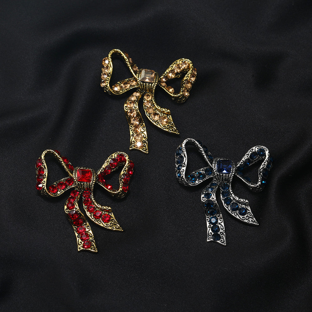 This eye-catching brooch features a classic bow design, crafted with an antiqued gold-tone metal base intricately adorned with vibrant red crystals. A large, faceted red gemstone anchors the center, while delicate filigree detailing adds vintage charm. Perfect for elevating blazers, scarves, or festive outfits, this bold piece brings a touch of glamorous retro style to any look. 04
