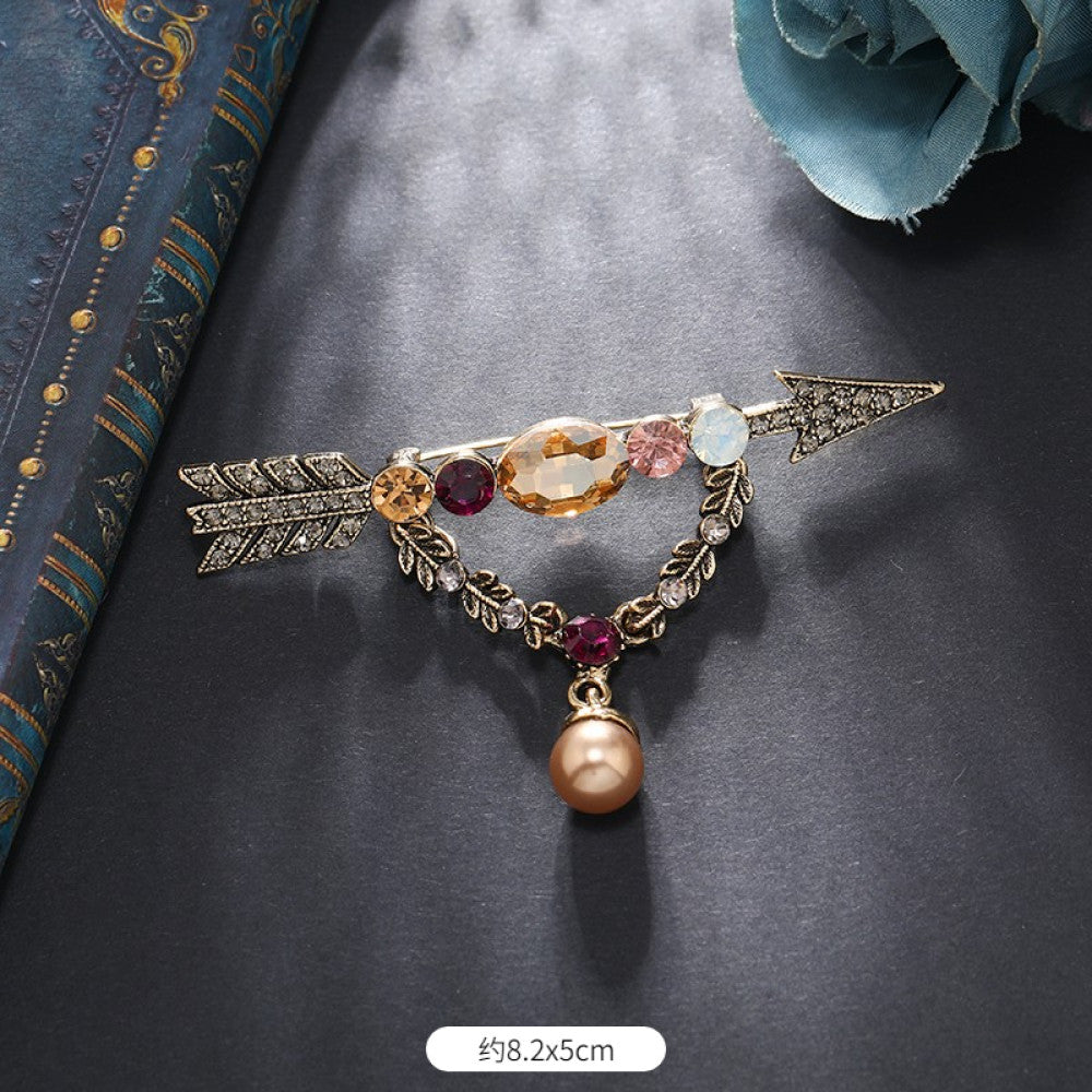 This vintage brooch set features an antiqued bronze base, adorned with pearls, colored crystals, and gemstones. The circular design sparkles with dense small crystals; the arrow-shaped piece carries a tribal vibe with a pearl pendant; the large gemstone brooch boasts a bold black stone with surrounding pearls and gems. Ideal for elevating the sophistication and vintage charm of your coats, blazers, or dresses. 06