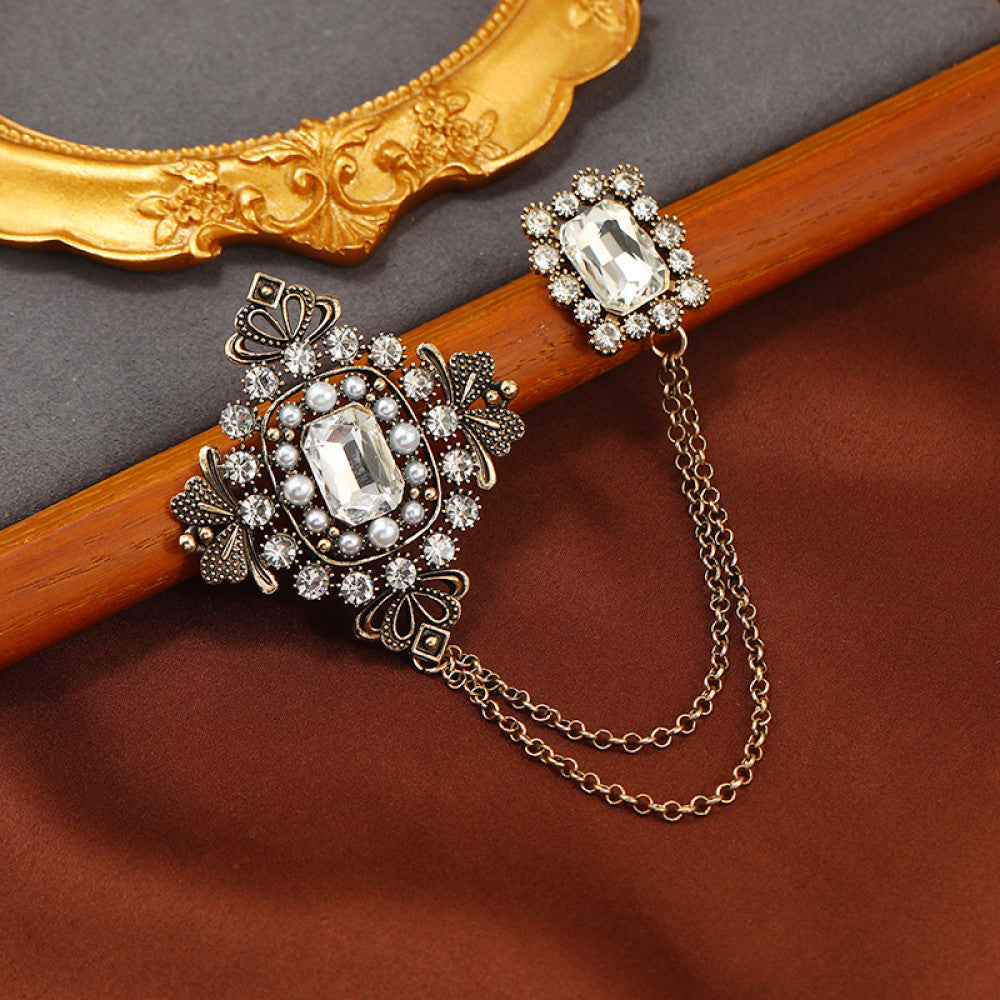 This vintage-style double brooch set features an ornate filigree design with a large emerald-green gem at its center, connected by delicate chains to a smaller matching brooch. Adorned with blue and white accents, it adds sophisticated antique charm to any outfit 01