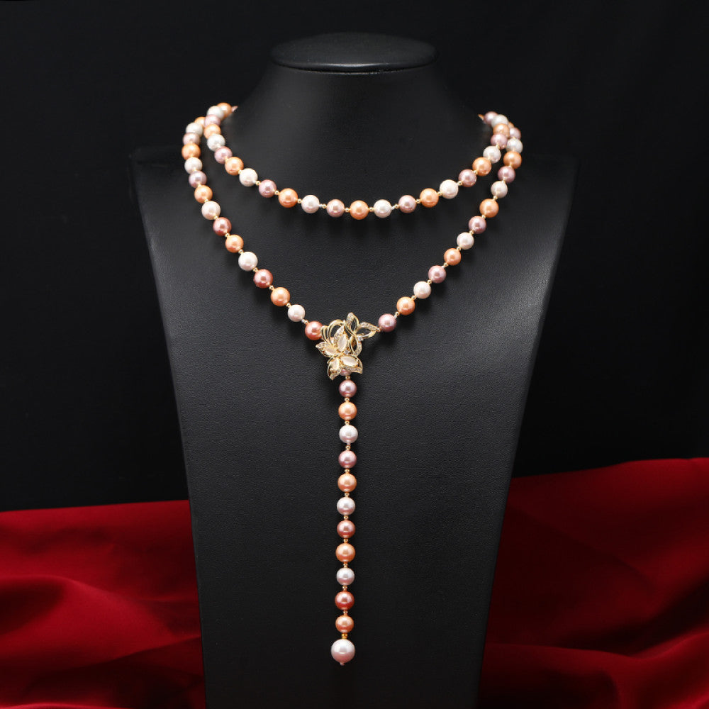 Elegant multi-colored pearl Y-necklace with gold floral accent, featuring layered strands and a drop pendant, ideal for vintage-inspired formal or special occasion wear, displayed on a black mannequin against a red fabric background