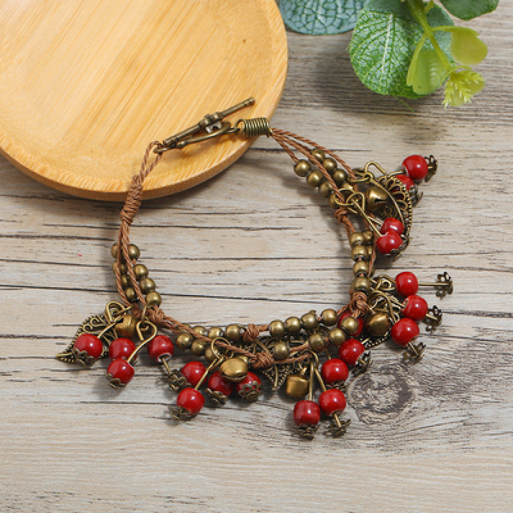 This vintage-style bracelet features a brown braided cord, adorned with antique bronze leaf charms and vibrant red berry-like beads, creating a nature-inspired, bohemian look. The toggle clasp ensures a secure fit, making it a striking accessory for any outfit 3