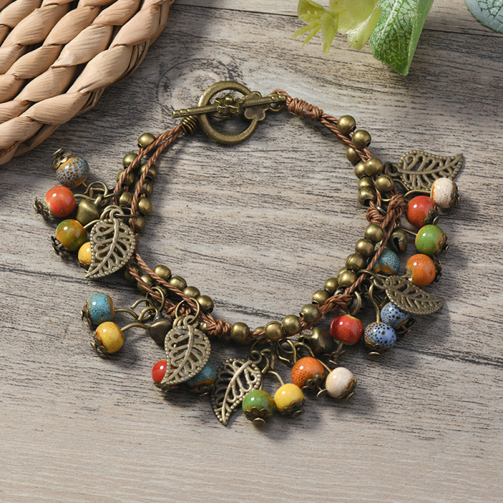 This vintage-style bracelet features a brown braided cord, adorned with antique bronze leaf charms and vibrant red berry-like beads, creating a nature-inspired, bohemian look. The toggle clasp ensures a secure fit, making it a striking accessory for any outfit 4