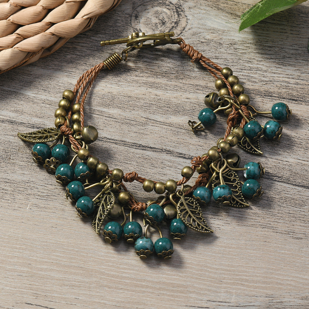 This vintage-style bracelet features a brown braided cord, adorned with antique bronze leaf charms and vibrant red berry-like beads, creating a nature-inspired, bohemian look. The toggle clasp ensures a secure fit, making it a striking accessory for any outfit 5