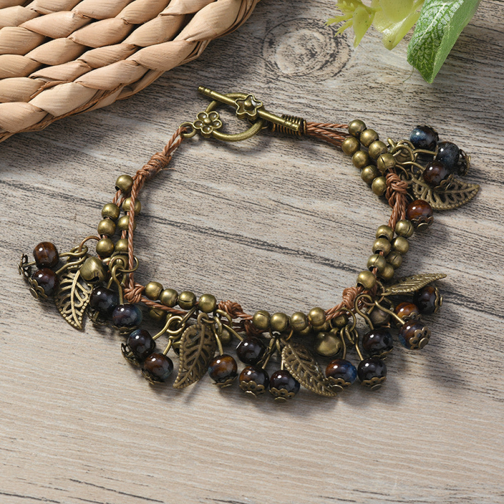 This vintage-style bracelet features a brown braided cord, adorned with antique bronze leaf charms and vibrant red berry-like beads, creating a nature-inspired, bohemian look. The toggle clasp ensures a secure fit, making it a striking accessory for any outfit 6