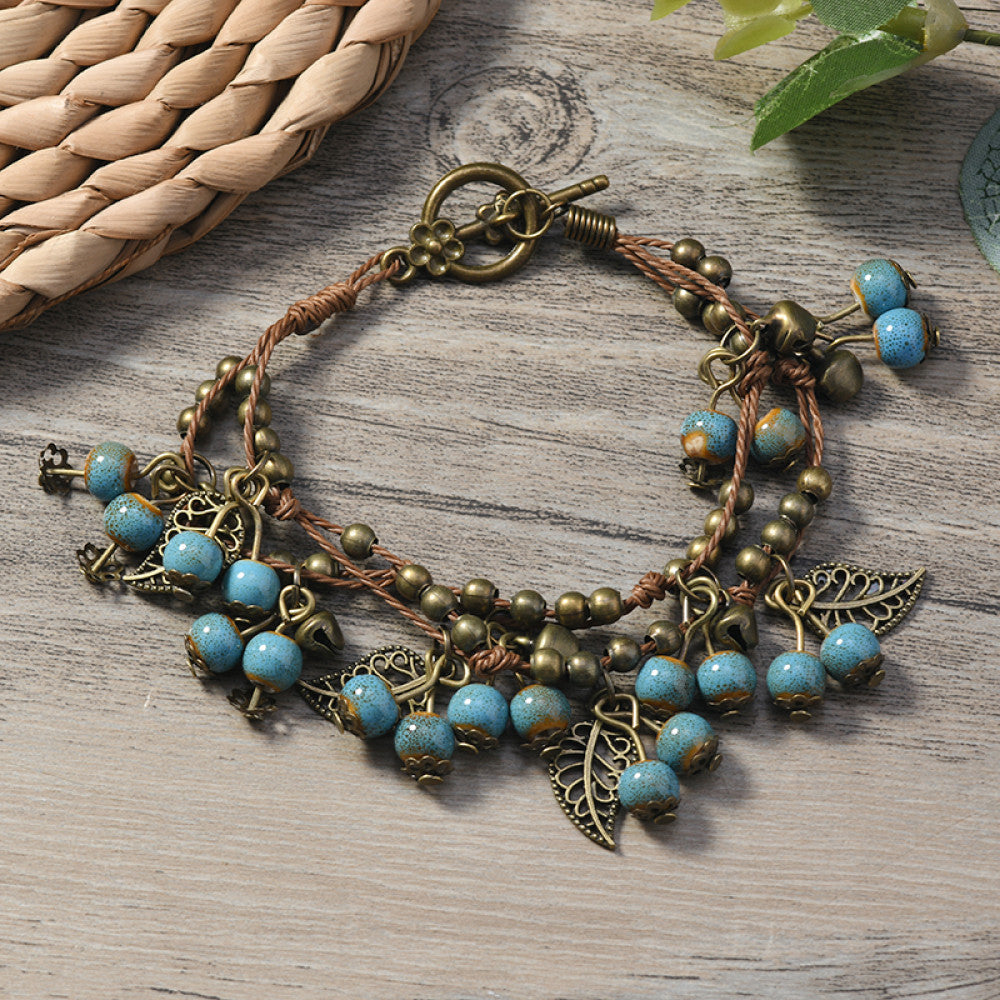 This vintage-style bracelet features a brown braided cord, adorned with antique bronze leaf charms and vibrant red berry-like beads, creating a nature-inspired, bohemian look. The toggle clasp ensures a secure fit, making it a striking accessory for any outfit 8