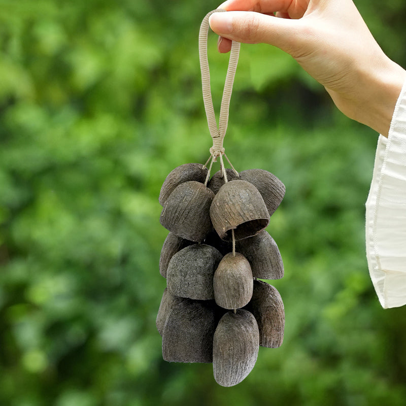 Hand holding dark bell‑shaped seed pod tassel, outdoor green foliage lifestyle shot | DIY Jade