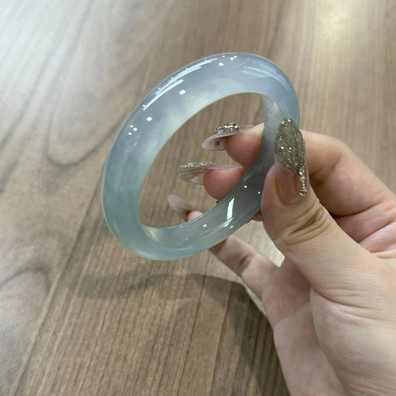 Icy light blue jade bangle close-up held by hand with manicured nails, showing crystal clear texture | DIY Jade